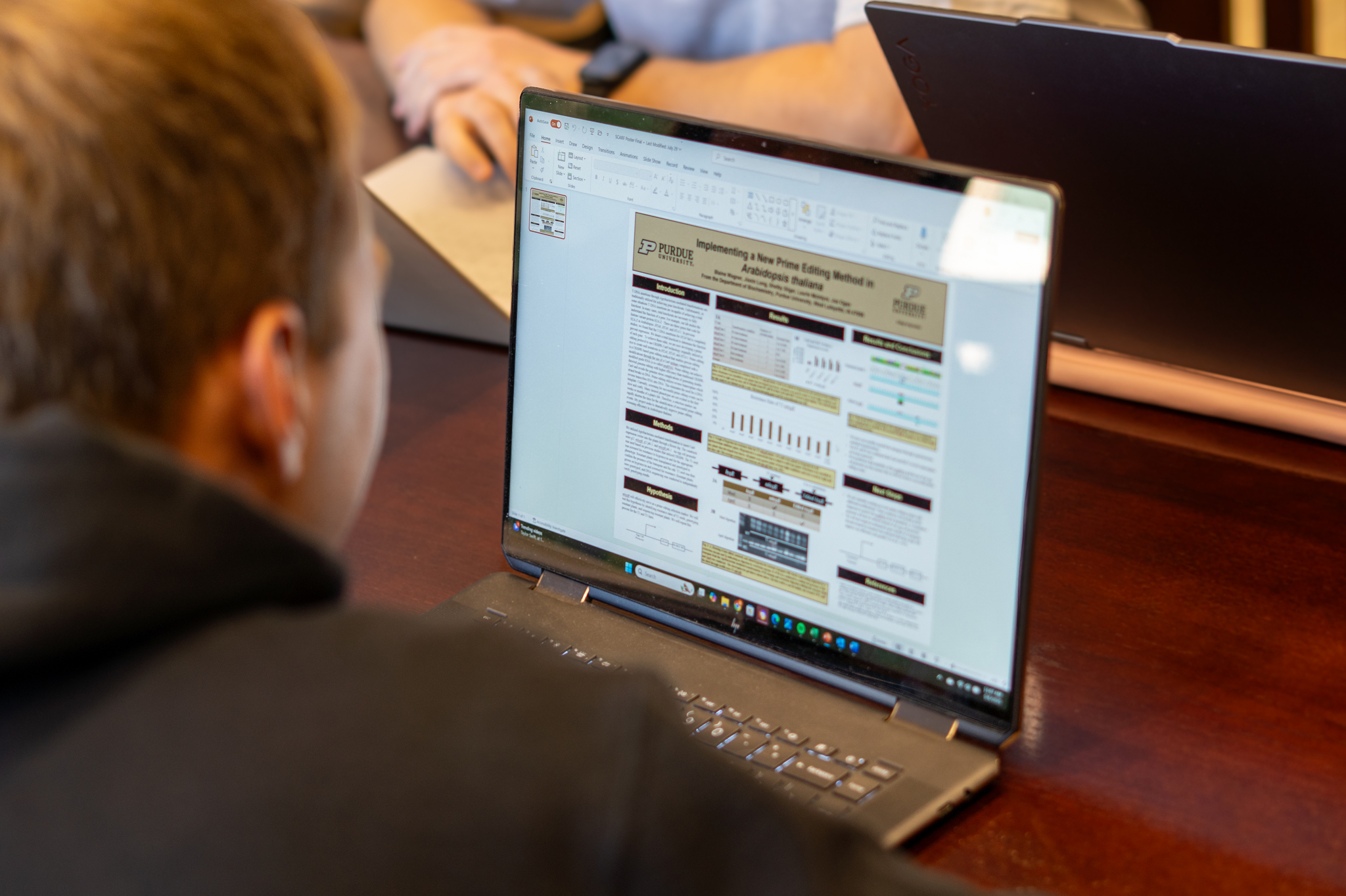 A shot over a students shoulder, who is looking at their laptop with an image of their research poster